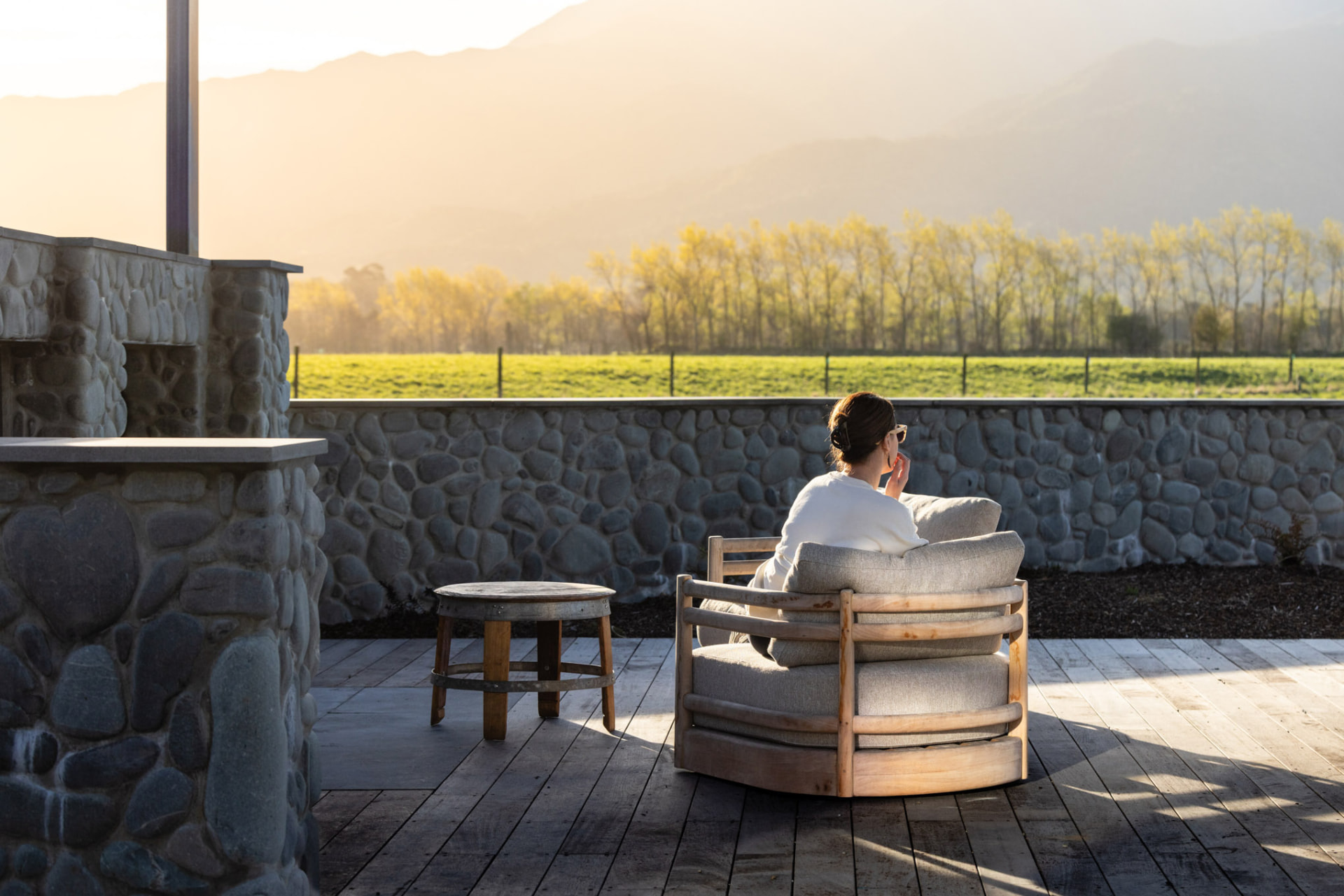 Guest relaxing by the outdoor fire at sunset with mountain views at Whakahā