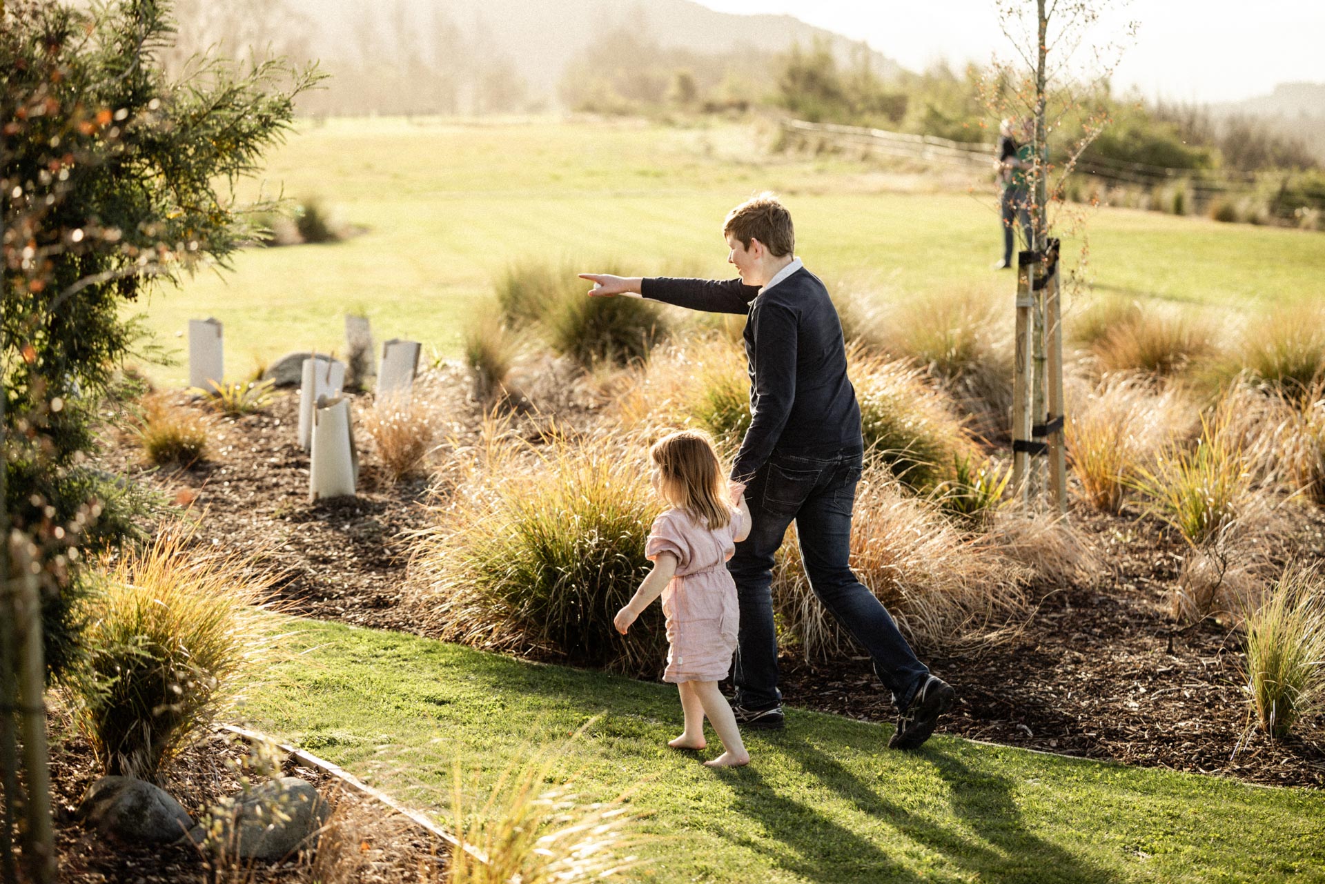 Parent and child walking through the tussock gardens at Whakahā at golden hour