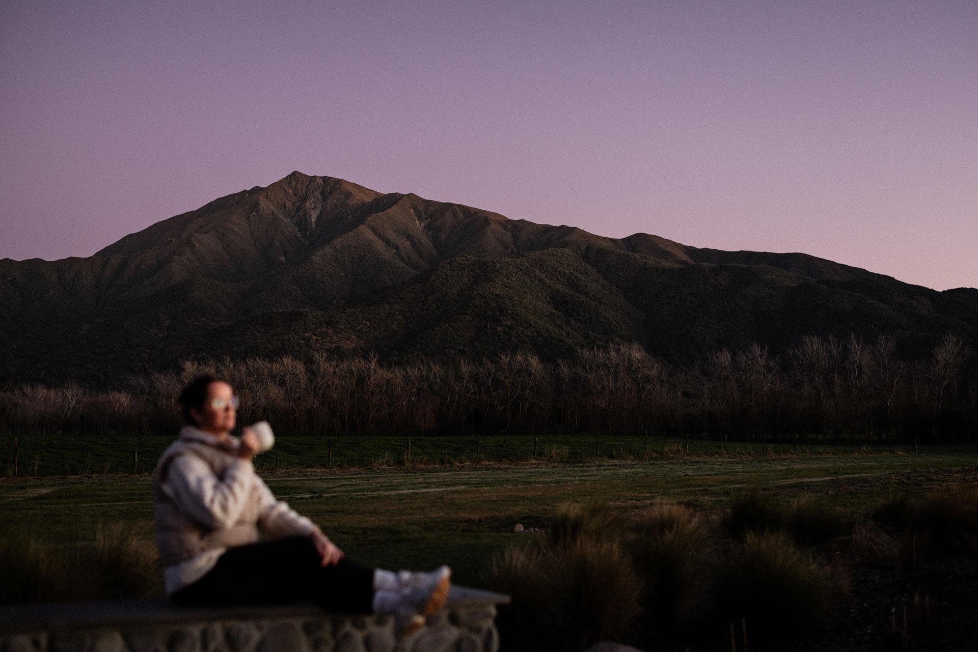 Guest watching Mt Peel from Whakahā at dusk with a warm drink