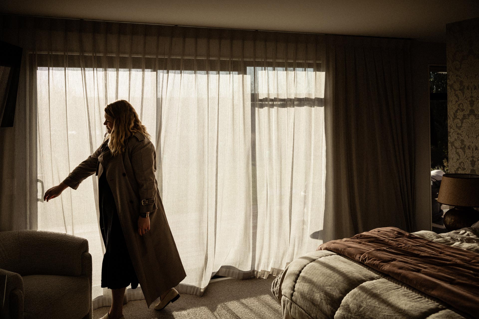 Guest drawing back the sheer curtains in the master suite at Whakahā